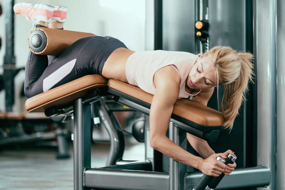 leg-curl-tumbado mujer trabajando los isquiotibilaes tumbada en máquina